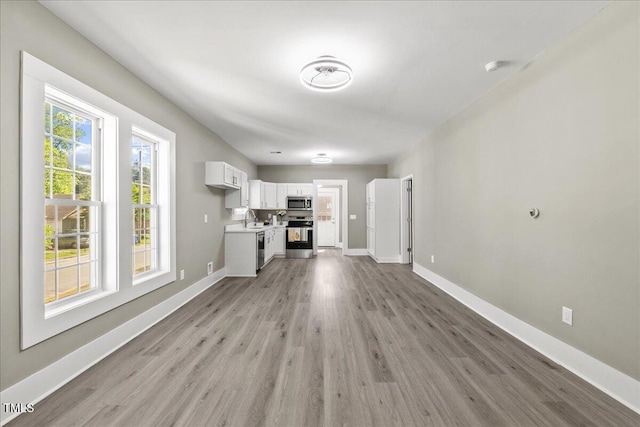 unfurnished living room with light wood-style flooring, baseboards, and a sink