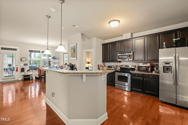 kitchen featuring appliances with stainless steel finishes, a breakfast bar area, wood finished floors, pendant lighting, and light stone countertops