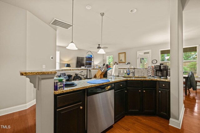 kitchen with stainless steel dishwasher, a sink, wood finished floors, light stone counters, and hanging light fixtures