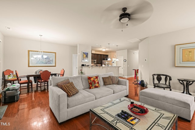 living room featuring ceiling fan, a chandelier, dark wood-type flooring, and baseboards