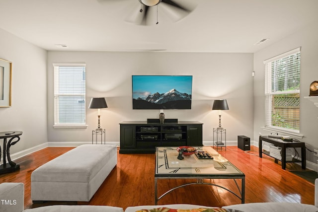 living area with healthy amount of natural light, wood finished floors, a ceiling fan, and baseboards