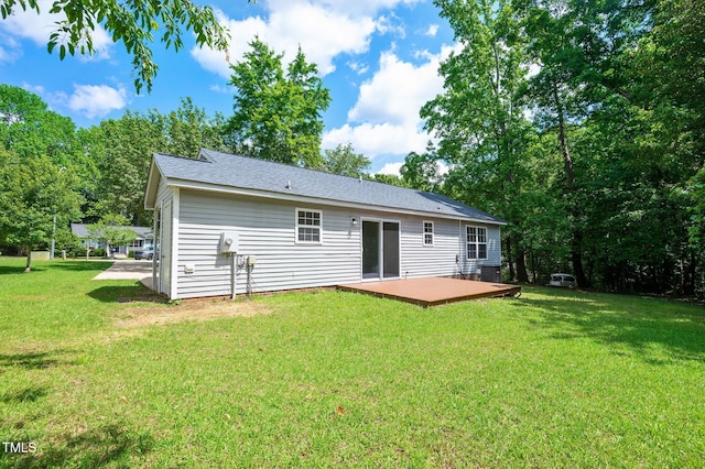 rear view of property featuring a wooden deck, a lawn, and roof with shingles