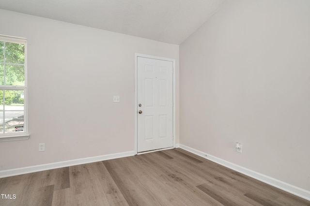 empty room with wood finished floors, baseboards, and vaulted ceiling