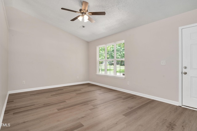 empty room with vaulted ceiling, wood finished floors, ceiling fan, a textured ceiling, and baseboards