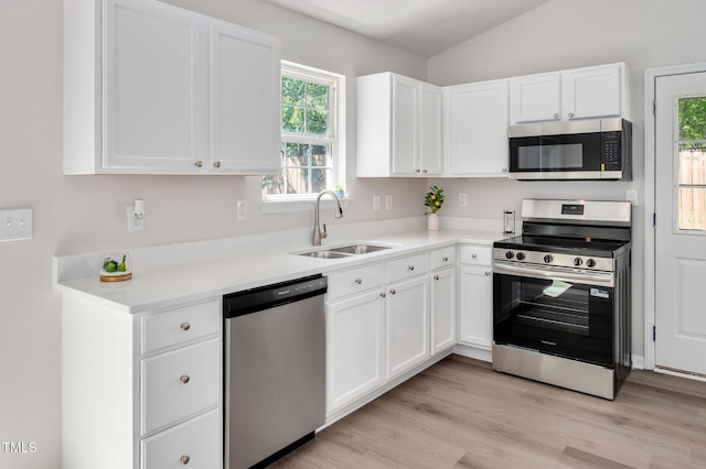 kitchen featuring stainless steel appliances, a sink, white cabinetry, and vaulted ceiling