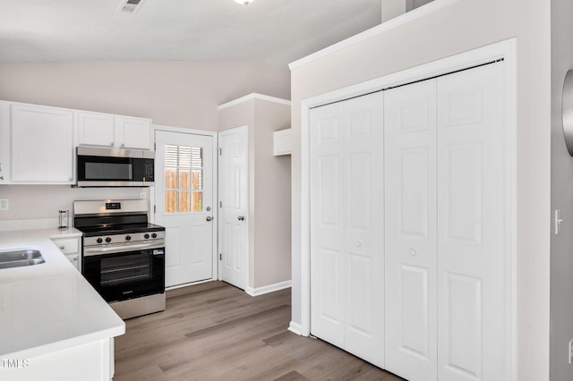 kitchen featuring stainless steel appliances, vaulted ceiling, white cabinetry, light countertops, and a sink