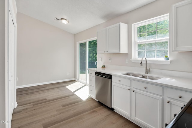 kitchen with stainless steel dishwasher, a sink, white cabinets, plenty of natural light, and vaulted ceiling