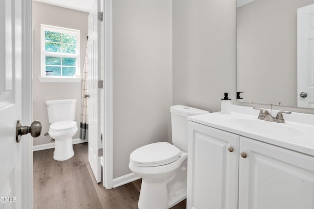 bathroom with toilet, wood finished floors, vanity, and baseboards