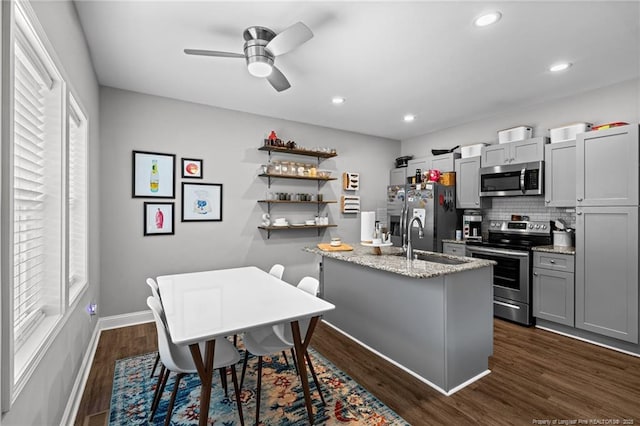 kitchen featuring stainless steel appliances, a sink, backsplash, ceiling fan, and baseboards