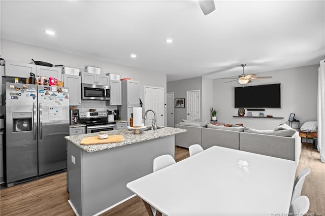 kitchen featuring appliances with stainless steel finishes, ceiling fan, a sink, a kitchen island with sink, and backsplash