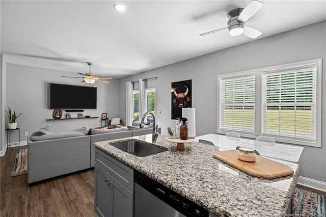 kitchen featuring ceiling fan, a sink, light stone countertops, dark wood-style flooring, and a kitchen island with sink