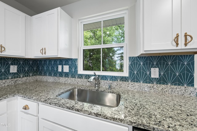 kitchen with a sink, white cabinetry, light stone counters, and tasteful backsplash