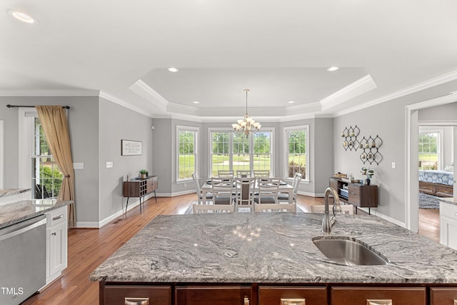 kitchen with a sink, a raised ceiling, an island with sink, light wood finished floors, and dishwasher