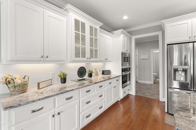 kitchen with appliances with stainless steel finishes, white cabinetry, glass insert cabinets, tasteful backsplash, and crown molding