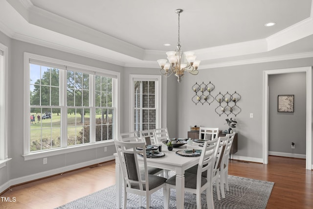 dining room with a raised ceiling, a chandelier, wood finished floors, ornamental molding, and baseboards