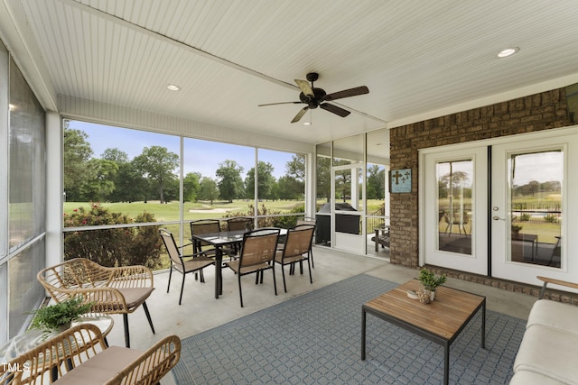 sunroom with a ceiling fan, view of golf course, outdoor dining space, and french doors