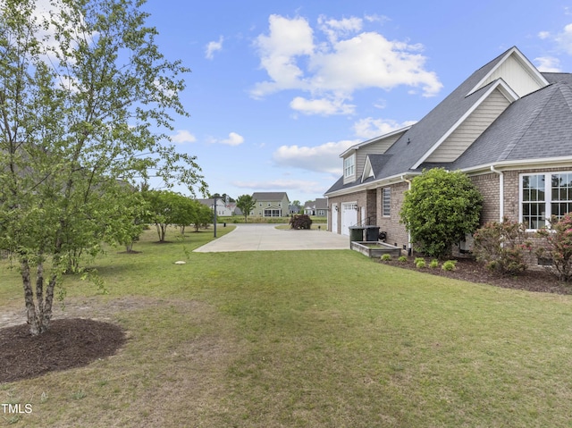 view of grassy yard with an attached garage and concrete driveway