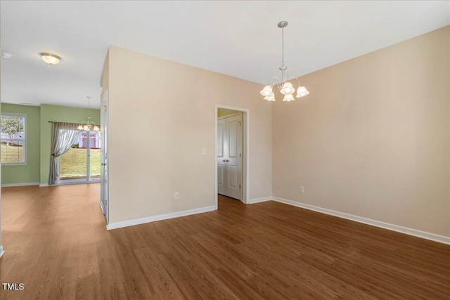 unfurnished room with a chandelier, wood finished floors, and baseboards