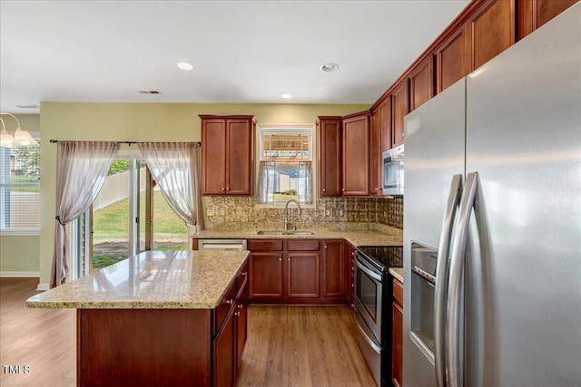 kitchen featuring appliances with stainless steel finishes, a sink, light wood finished floors, tasteful backsplash, and light stone countertops