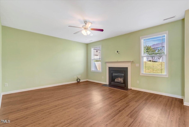 unfurnished living room featuring wood finished floors, a glass covered fireplace, ceiling fan, and baseboards