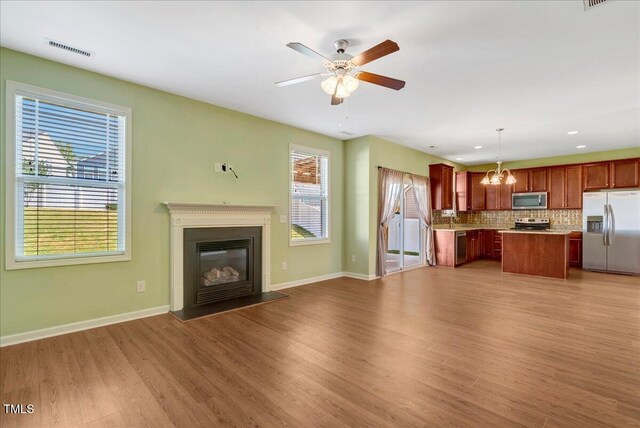 unfurnished living room with a chandelier, wood finished floors, a ceiling fan, baseboards, and a glass covered fireplace
