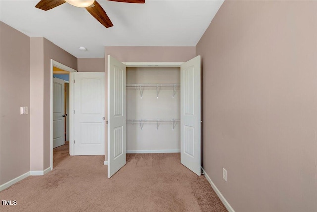 unfurnished bedroom featuring light colored carpet, baseboards, a closet, and a ceiling fan