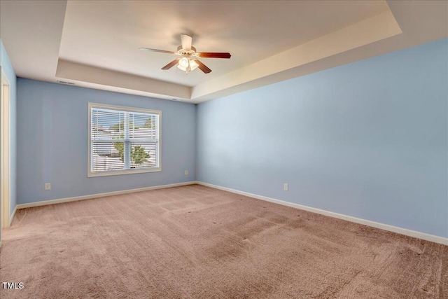 carpeted spare room with a tray ceiling, ceiling fan, and baseboards