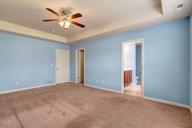 unfurnished bedroom featuring light colored carpet, baseboards, a raised ceiling, and ensuite bath