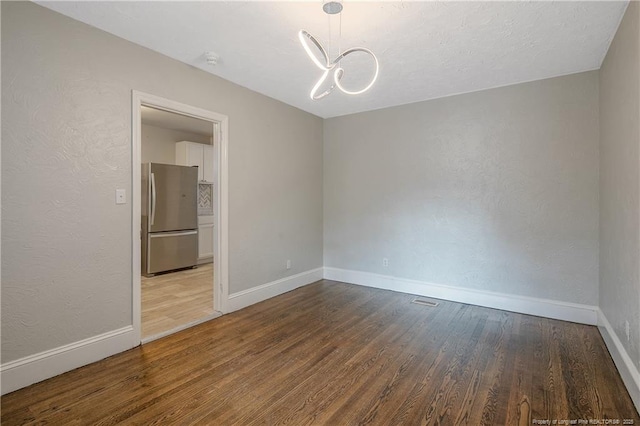empty room with wood finished floors, baseboards, a chandelier, and a textured wall
