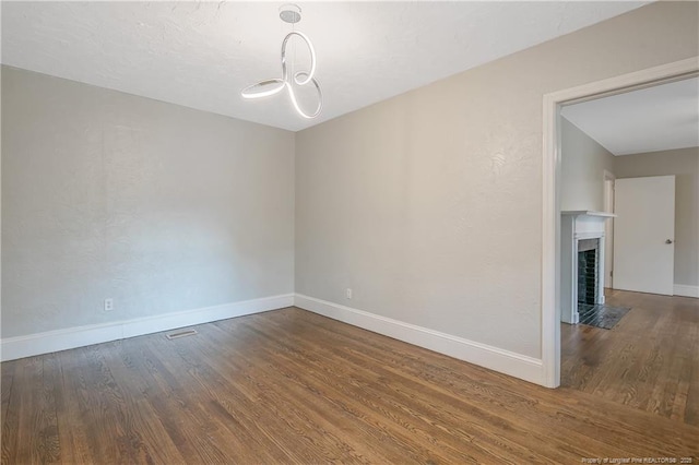 unfurnished room with wood finished floors, baseboards, a fireplace with flush hearth, and a chandelier