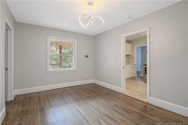 unfurnished bedroom with wood finished floors, a chandelier, and baseboards