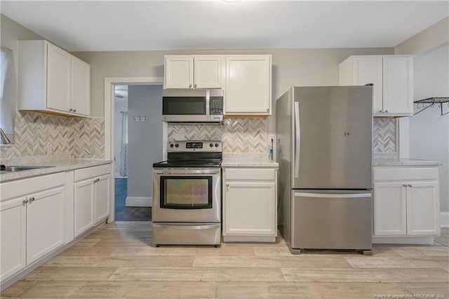 kitchen with appliances with stainless steel finishes, a sink, tasteful backsplash, and white cabinets