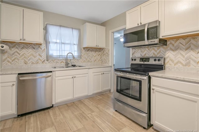 kitchen with stainless steel appliances, a sink, tasteful backsplash, white cabinets, and light wood finished floors