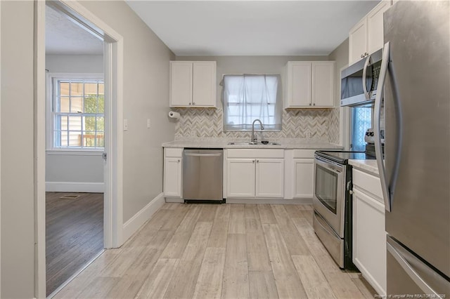 kitchen with stainless steel appliances, a sink, light wood-type flooring, and backsplash