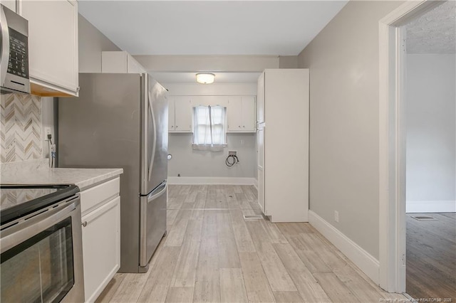 kitchen featuring stainless steel appliances, light countertops, white cabinetry, backsplash, and light wood finished floors