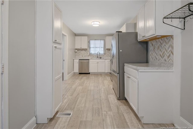 kitchen featuring appliances with stainless steel finishes, a sink, light countertops, backsplash, and white cabinets