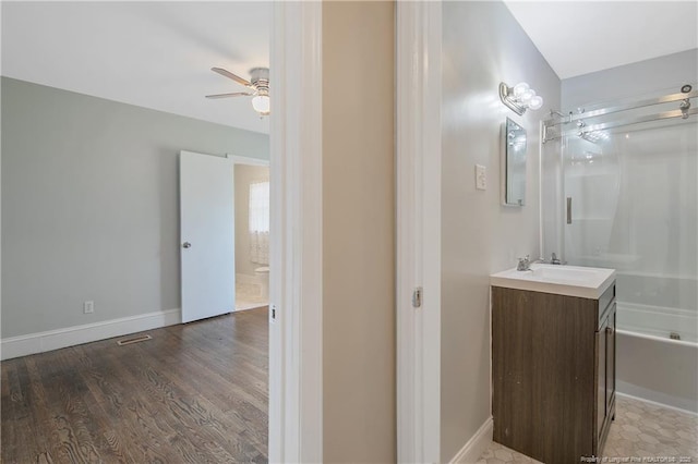bathroom with ceiling fan, vanity, wood finished floors, bathing tub / shower combination, and baseboards