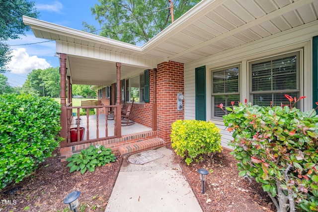 entrance to property with a porch and brick siding