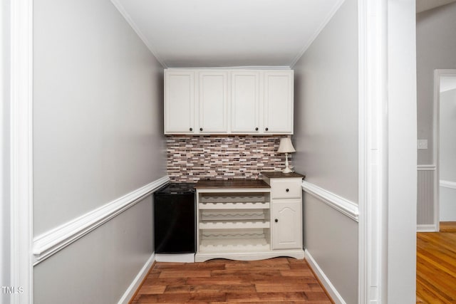 bar area featuring decorative backsplash, light wood-style flooring, crown molding, and baseboards