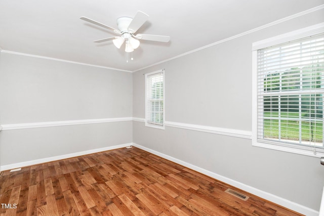 empty room with healthy amount of natural light, wood finished floors, baseboards, and crown molding