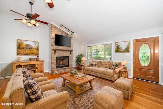 living room with vaulted ceiling, ceiling fan, wood finished floors, a brick fireplace, and rail lighting