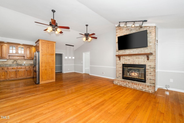 unfurnished living room with light wood-style floors, ceiling fan, a brick fireplace, lofted ceiling, and a sink