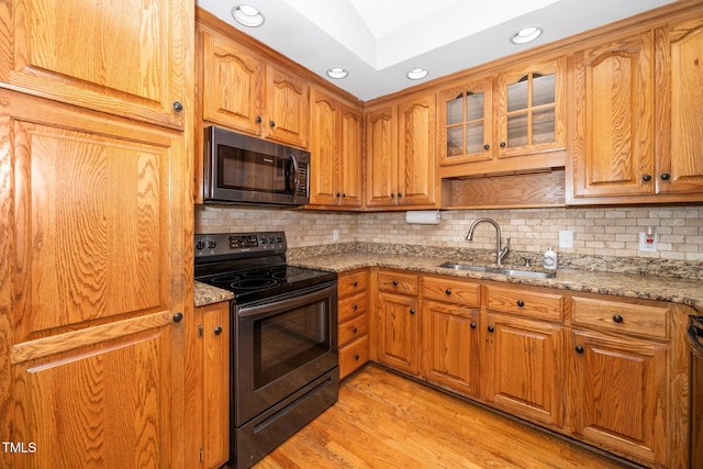 kitchen featuring black / electric stove, a sink, light stone counters, brown cabinetry, and recessed lighting