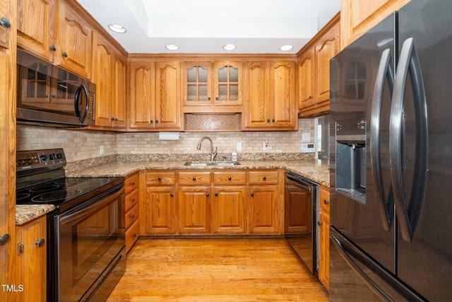 kitchen featuring black appliances, a sink, brown cabinetry, recessed lighting, and light stone counters