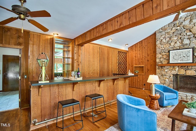 kitchen with wood walls, ceiling fan, brown cabinetry, wood finished floors, and lofted ceiling