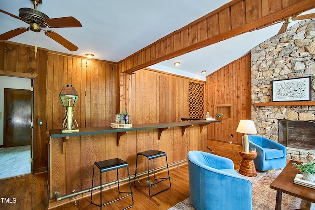 bar area with wood walls, ceiling fan, wood finished floors, a fireplace, and vaulted ceiling
