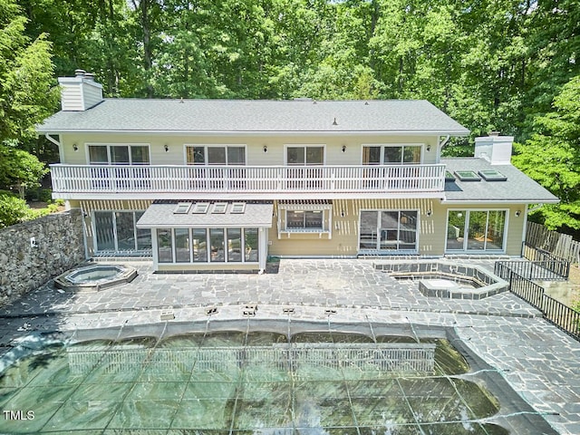 back of property with an in-ground hot tub, a balcony, a chimney, and a patio area