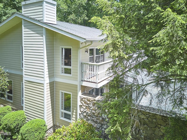 view of property exterior with a chimney, a balcony, roof with shingles, and stone siding