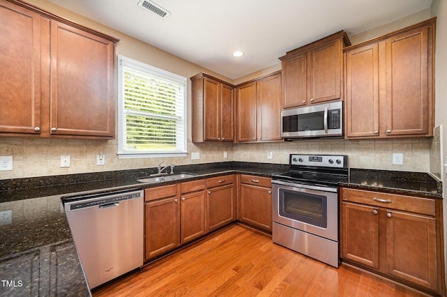 3403 Cardinal Lake Dr, Durham, NC 27704 - kitchen featuring appliances with stainless steel finishes, light wood finished floors, a sink, backsplash, and dark stone countertops
