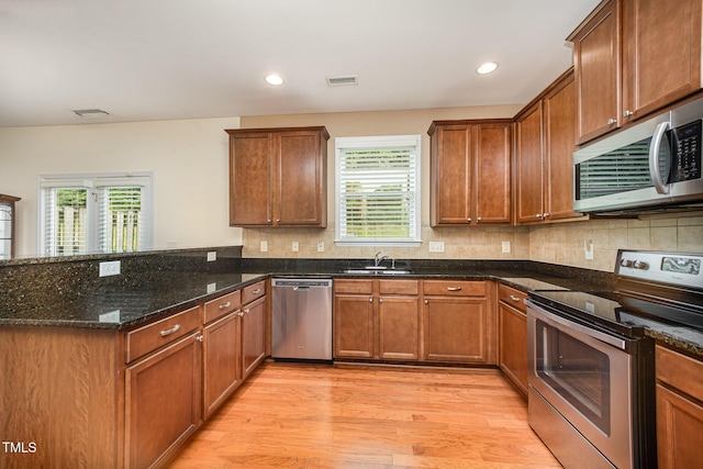 3403 Cardinal Lake Dr, Durham, NC 27704 - kitchen with appliances with stainless steel finishes, a peninsula, a sink, light wood finished floors, and dark stone countertops